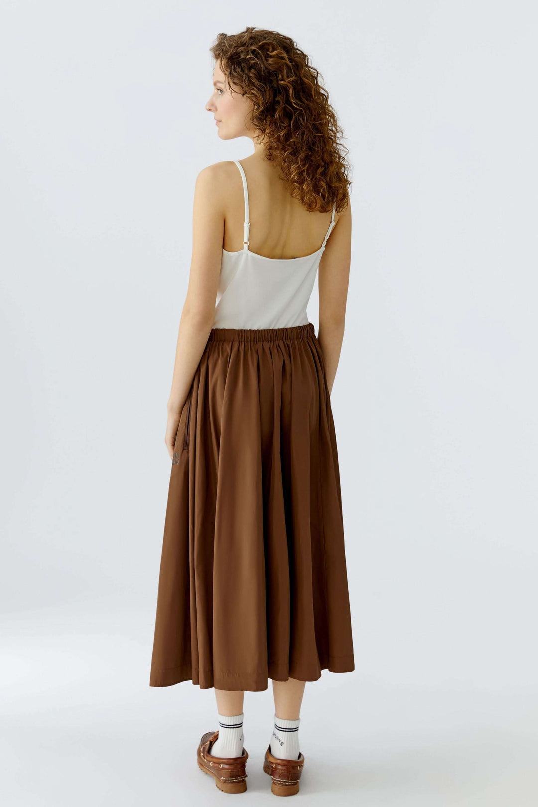 Jupe midi fluide marron avec taille élastique et cordon, offrant confort et mouvement naturel, portée avec un haut blanc simple.