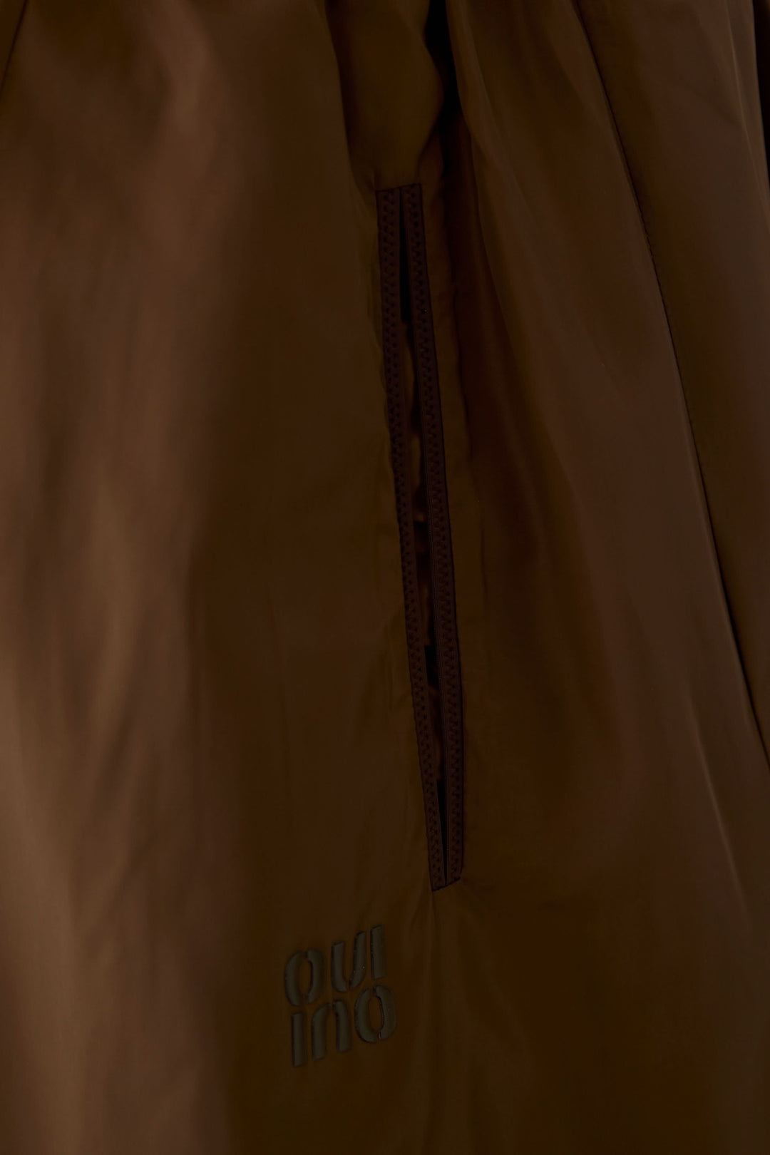 Détail sur le tissu marron de la jupe midi fluide avec poche latérale et logo cousu.