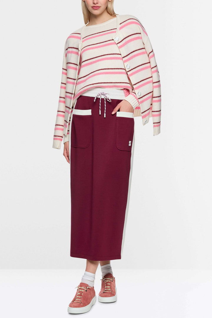 Jupe midi sportive bordeaux avec poches et cordon, détails contrastés, logo Marc Cain, portée avec un cardigan rayé.