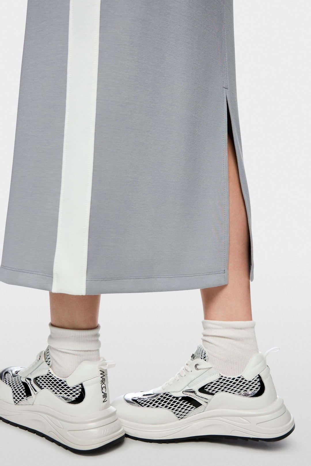 Jupe midi sportive avec bandes contrastées et fente arrière, mise en scène avec sneakers, mettant en valeur le style et le confort.
