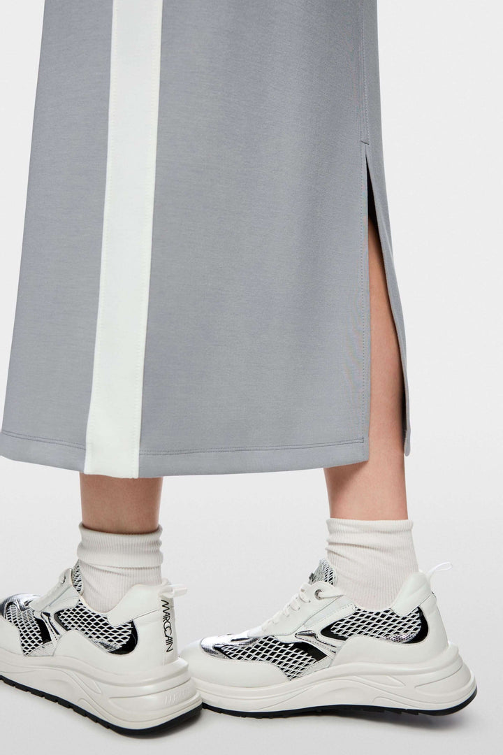 Jupe midi sportive avec bandes contrastées et fente arrière, mise en scène avec sneakers, mettant en valeur le style et le confort.