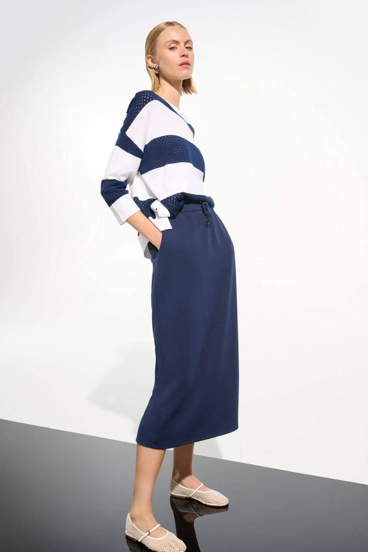 Femme portant une jupe midi à taille coulissante avec un chandail rayé, décontractée et chic, longueur mi-mollet, mode moderne.