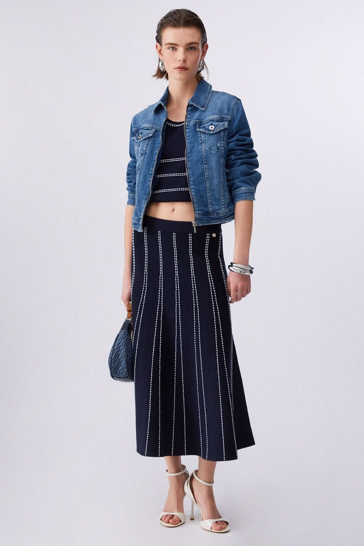 Jupe midi évasée à motif rayé portée avec une veste en jean et des sandales blanches.