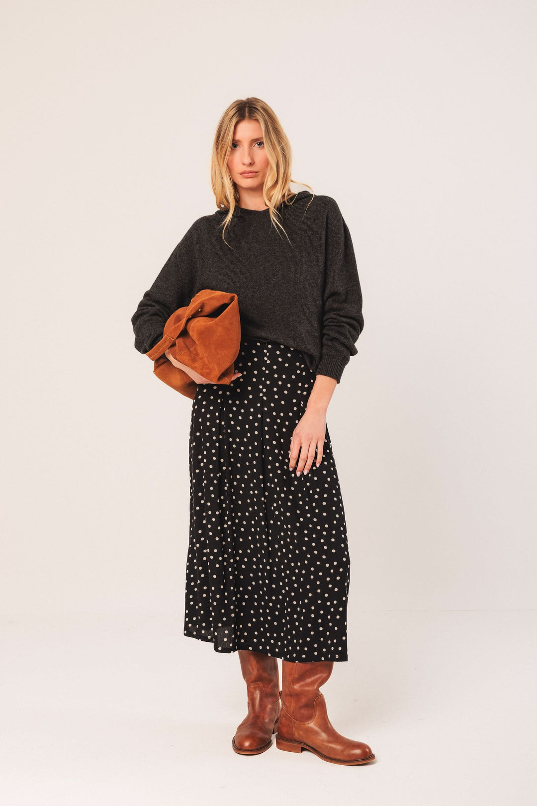 Femme portant une jupe à pois noire et un pull gris, avec un sac marron, style décontracté et élégant.