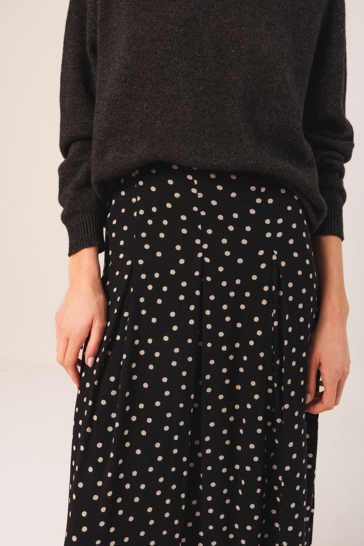 Jupe midi fluide à pois contrastés portée avec un chandail noir, offrant un look décontracté et élégant.
