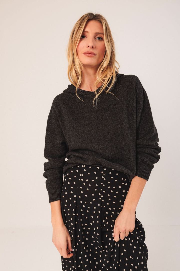 Femme portant un chandail noir avec une jupe midi à pois, style décontracté et élégant.