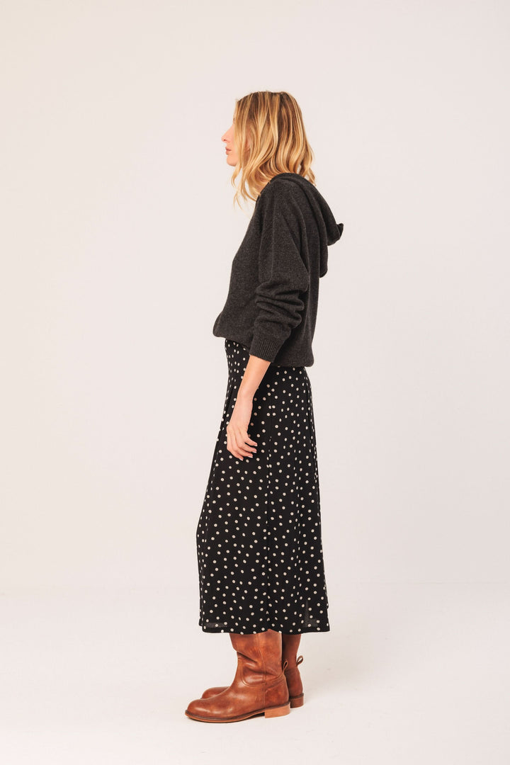 Femme en jupe midi à pois, associée à un chandail noir et des bottes marron, style décontracté.