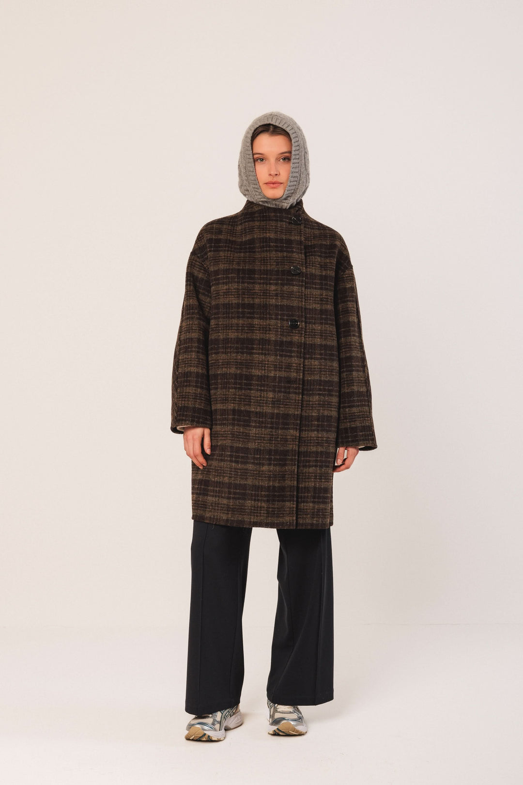 Manteau à carreaux oversize, col à revers, porté avec pantalon fluide et accessoires modernes.