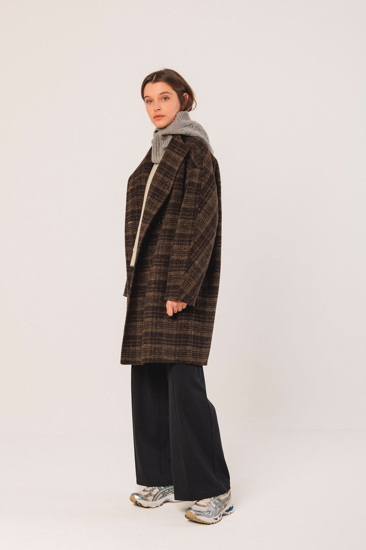 Manteau à carreaux oversize élégant, col à revers, porté avec un pull gris et pantalon fluide.