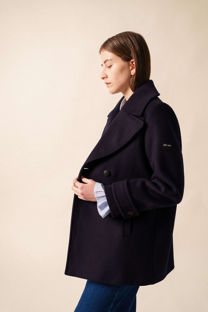 Femme portant le Manteau chic STE ROMY noir, avec encolure en V et grand col, montrant des boutons avant et manches élégantes.