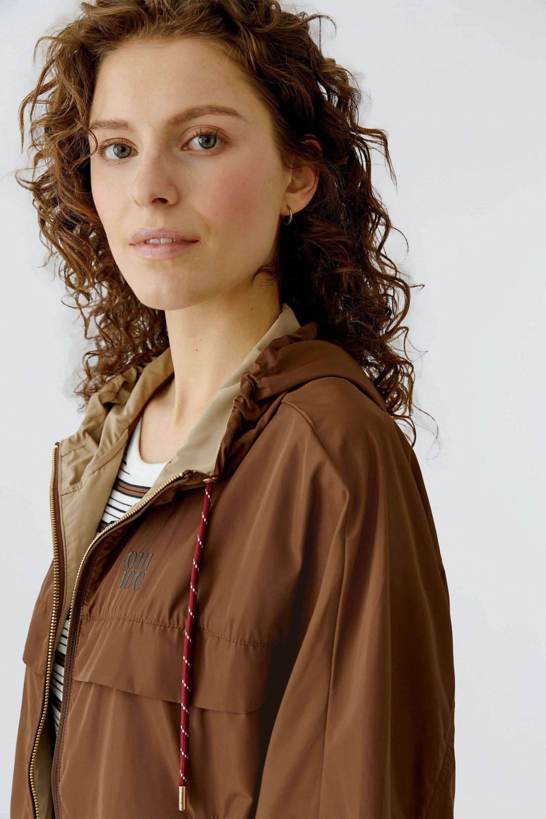Femme portant un manteau léger à capuchon brun avec capuchon intégré et cordon ajustable.