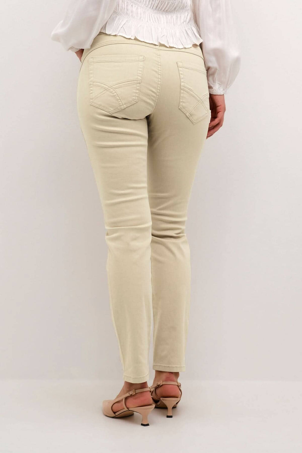 Pantalon beige à pleine longueur vu de dos, avec poches arrières et coupe régulière, porté avec des chaussures à talons.