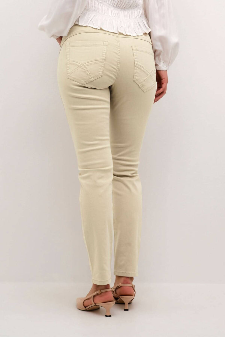 Pantalon beige à pleine longueur vu de dos, avec poches arrières et coupe régulière, porté avec des chaussures à talons.