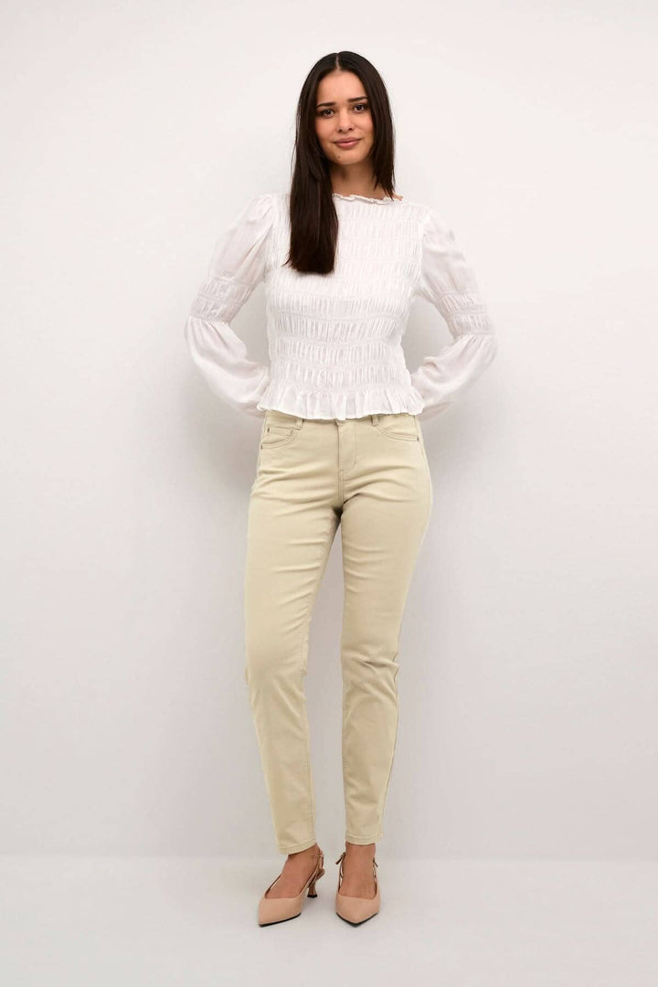 Femme portant un pantalon beige à pleine longueur avec une blouse blanche, parfait pour l&