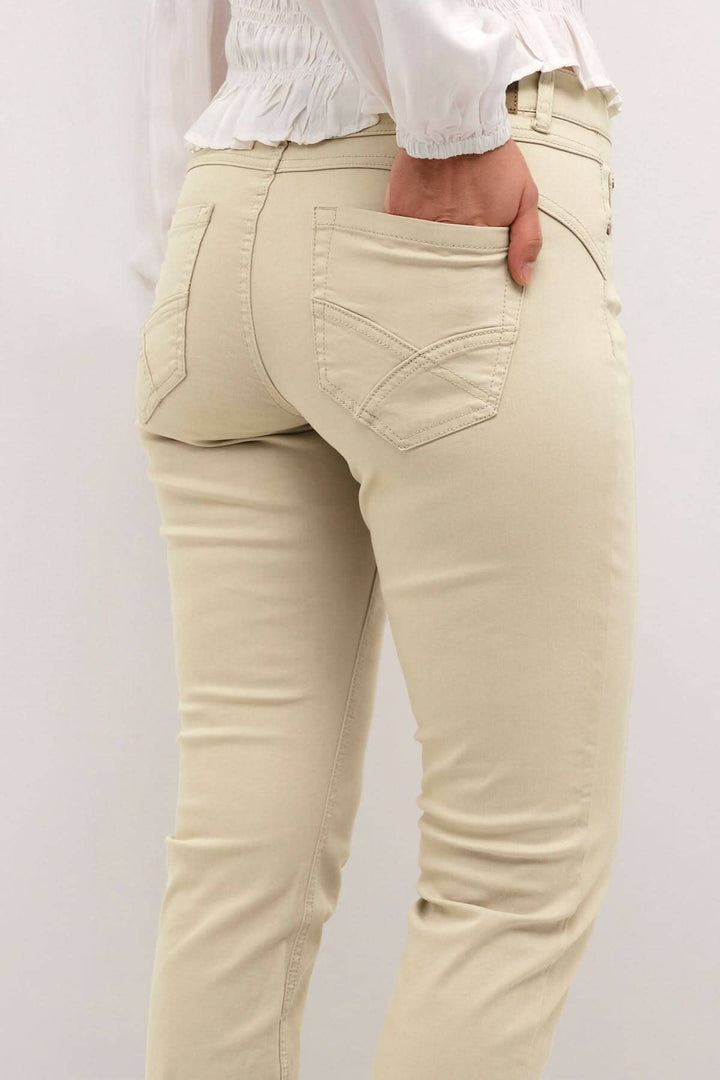 Femme portant un pantalon beige avec poches arrière, montrant la coupe régulière et le style décontracté.