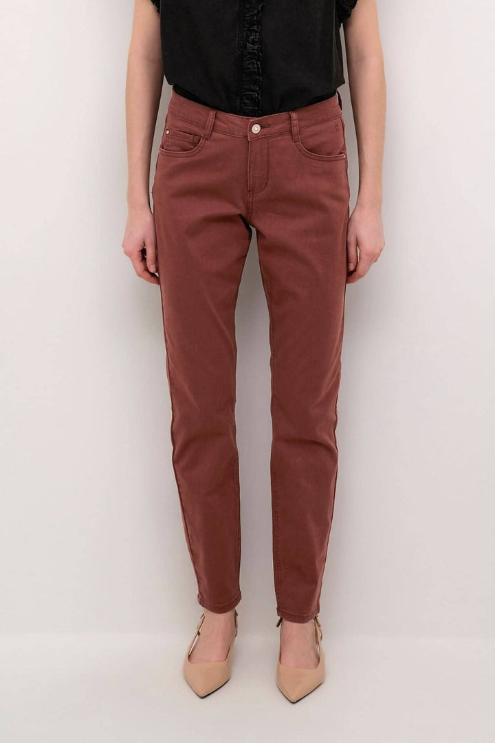 Pantalon Ann en couleur rouille, coupe régulière, poches avant et arrière, porté avec un top noir.