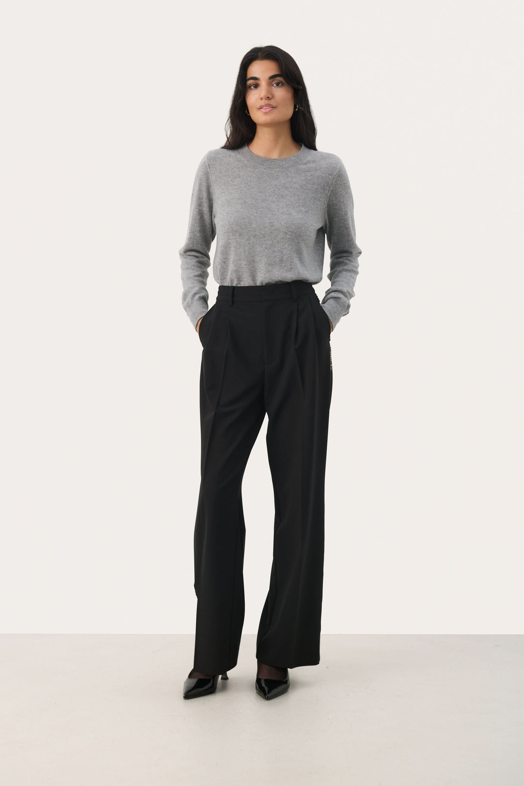 Femme portant un pantalon noir large avec une bande dorée, combiné avec un pull gris élégant.