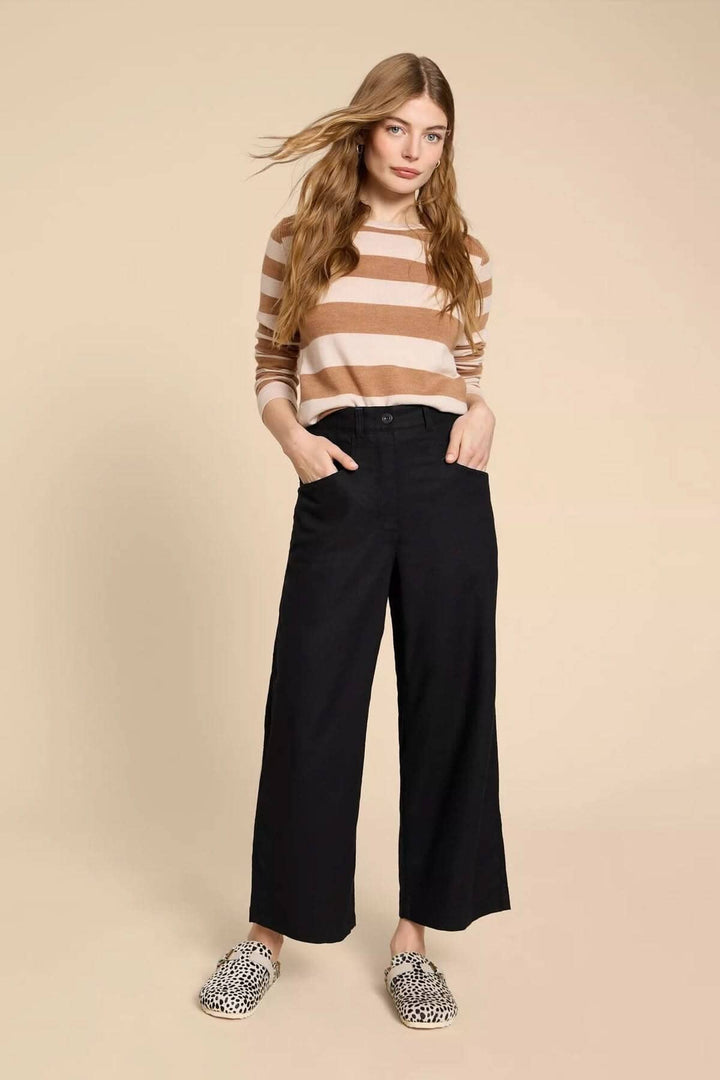 Femme portant le pantalon Harper à jambe large, avec un pull rayé, pose devant un fond neutre.