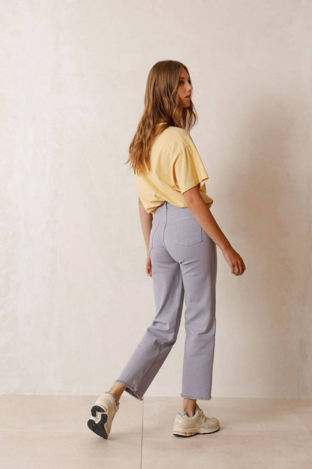 Femme avec un t-shirt jaune et un pantalon court bleu associé à des baskets, affichant un look décontracté et moderne.