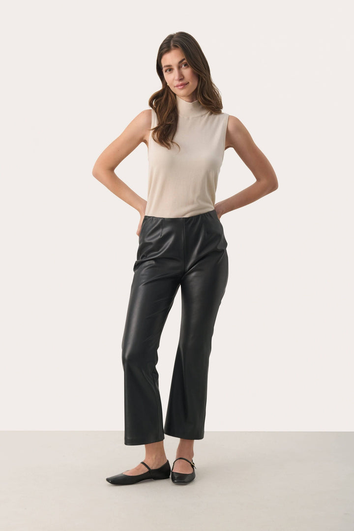 Pantalon noir en simili cuir, coupe évasée, taille haute, porté avec un haut beige, pour un look urbain et moderne.