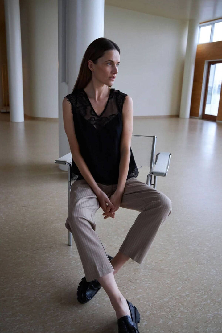 Femme portant un haut noir en dentelle et un pantalon Stella rayé, dans un espace moderne.