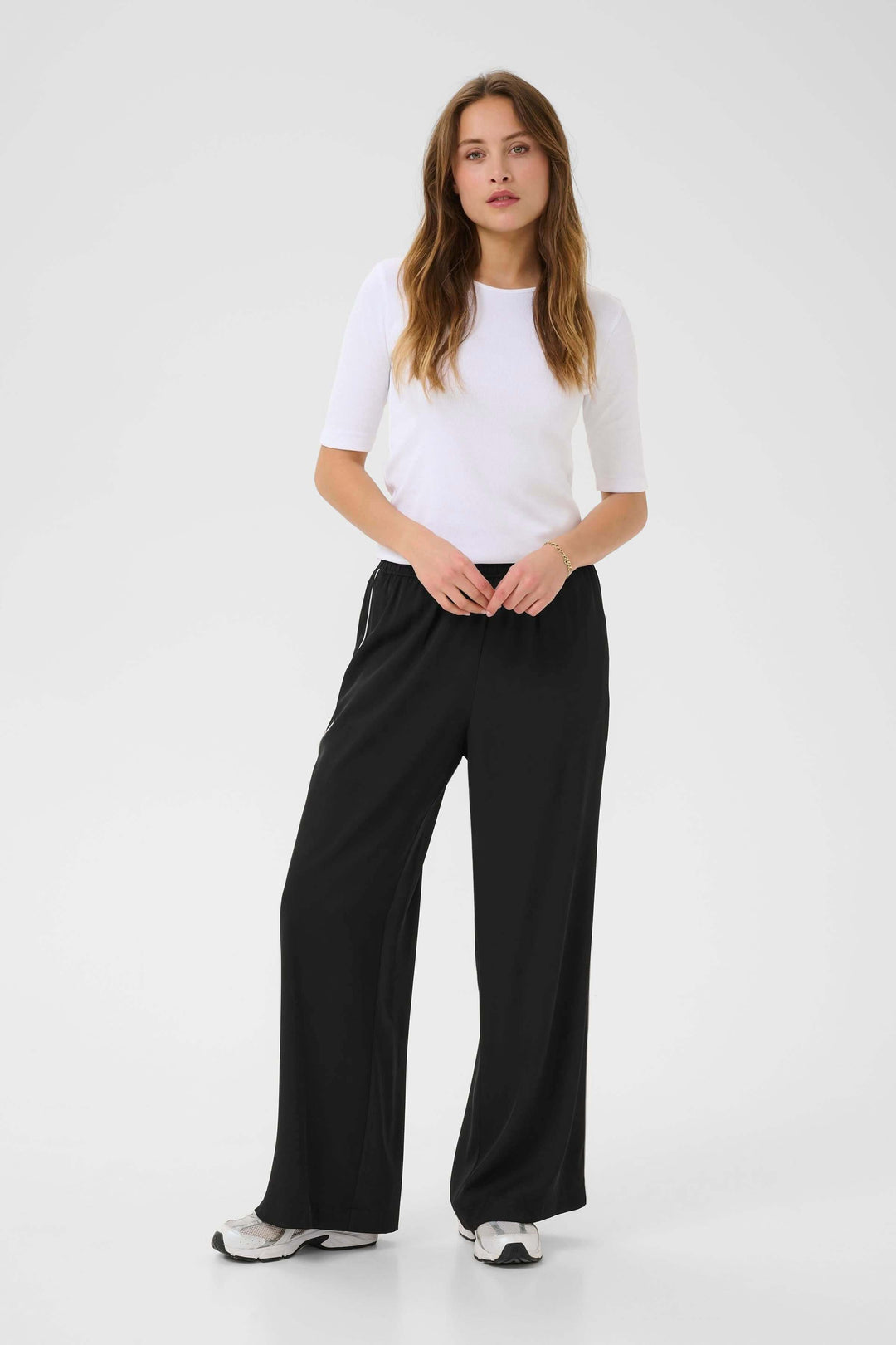 Femme portant le Pantalon Tessa fluide à jambe large, associé à un t-shirt blanc avec des baskets noires.