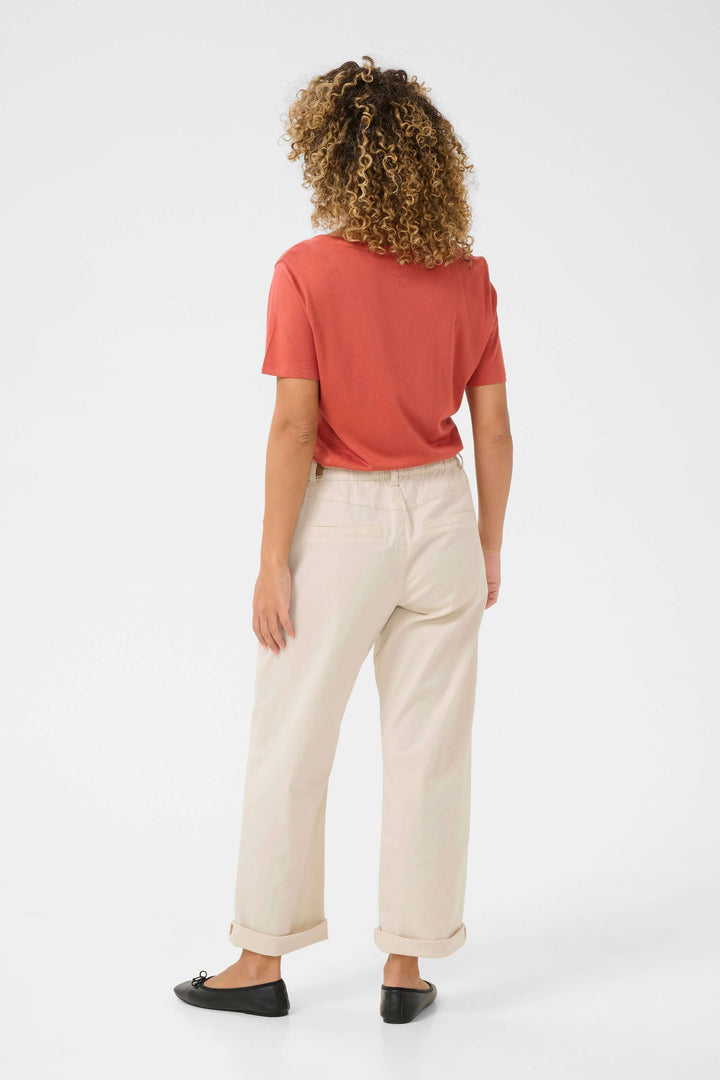 Femme avec t-shirt rouge et pantalon léger beige, vue de dos, pour style décontracté et estival.