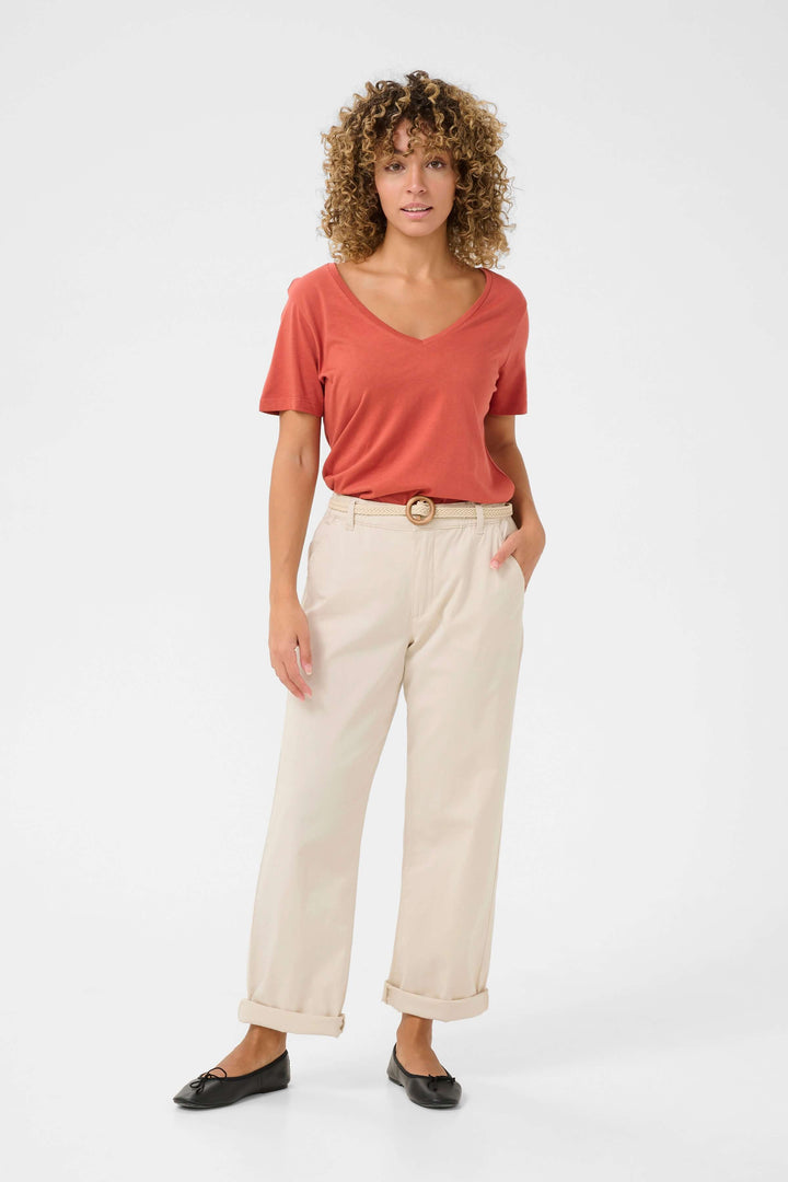 Femme portant un pantalon en toile légère et un t-shirt, style décontracté avec ceinture tressée, look estival.