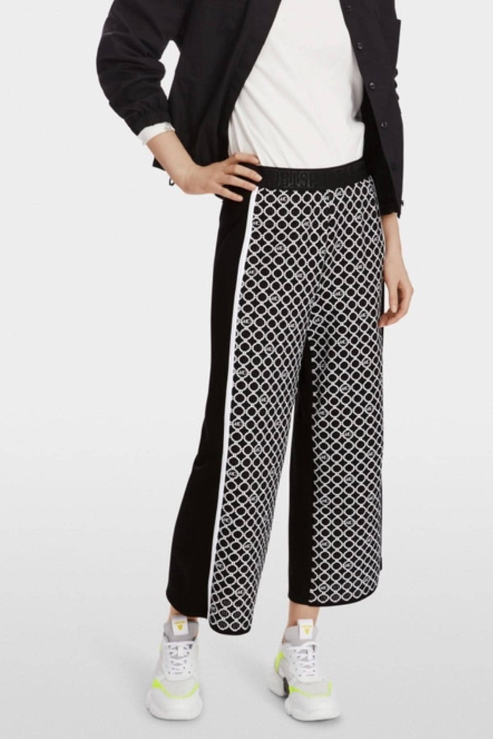 Pantalon WUSU noir et blanc à motif de chaînes, avec ceinture élastique, porté avec des baskets blanches.