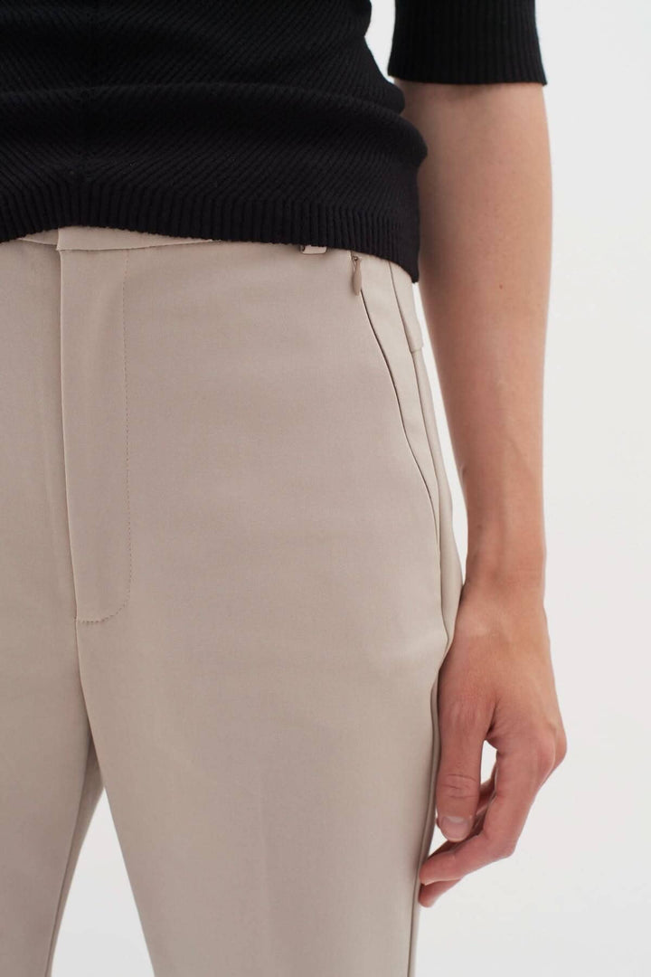 Détail du pantalon Ziggi beige, coupe ajustée avec poches zippées, porté avec un pull noir