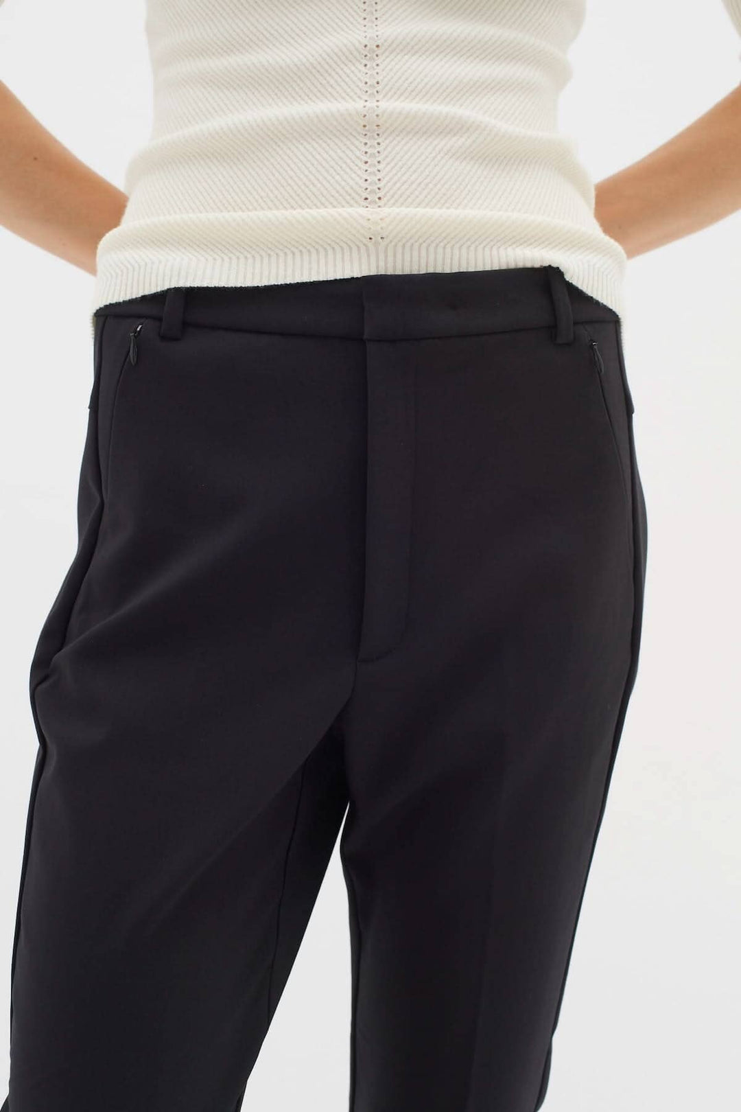 Pantalon Ziggi noir avec coupe ajustée et poches zippées, porté avec un haut blanc, style décontracté et élégant.