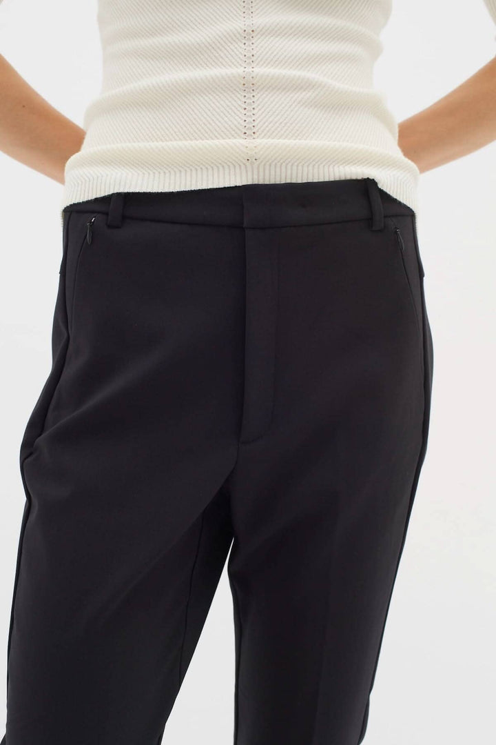 Pantalon Ziggi noir avec coupe ajustée et poches zippées, porté avec un haut blanc, style décontracté et élégant.