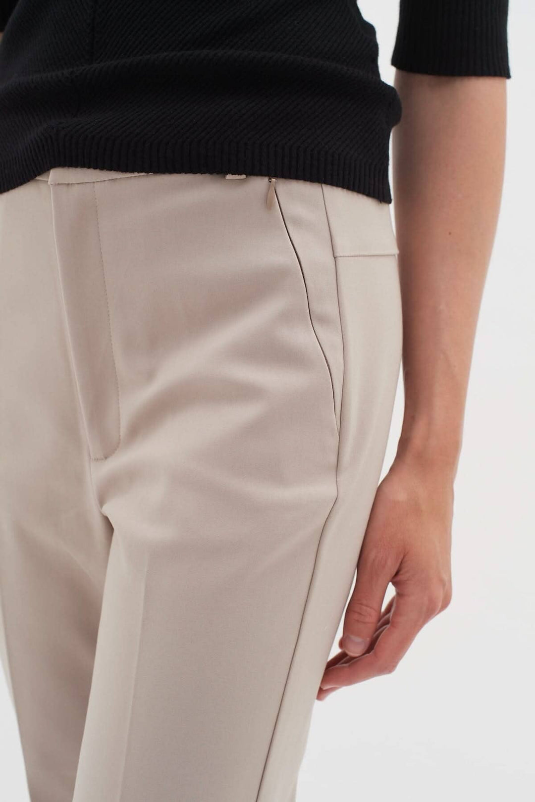 Détail du pantalon Ziggi beige avec poches zippées et coupe ajustée, associé à un haut noir.