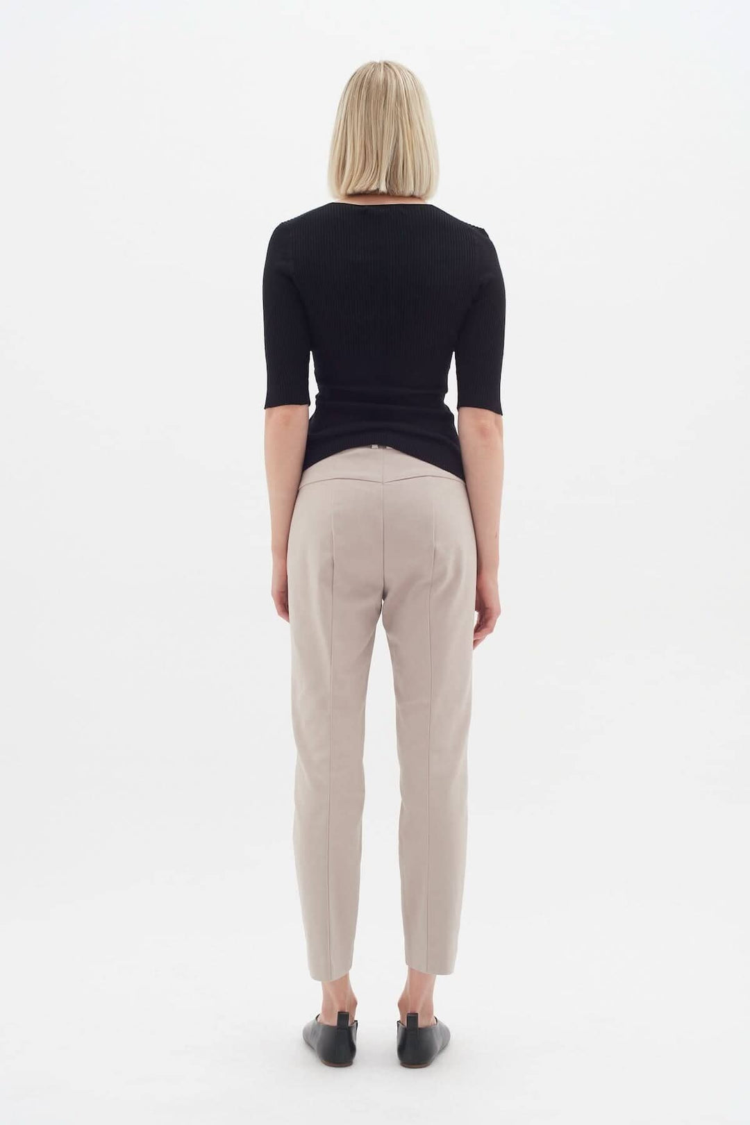 Femme vue de dos portant le pantalon Ziggi beige, avec un haut noir élégant et des chaussures noires.
