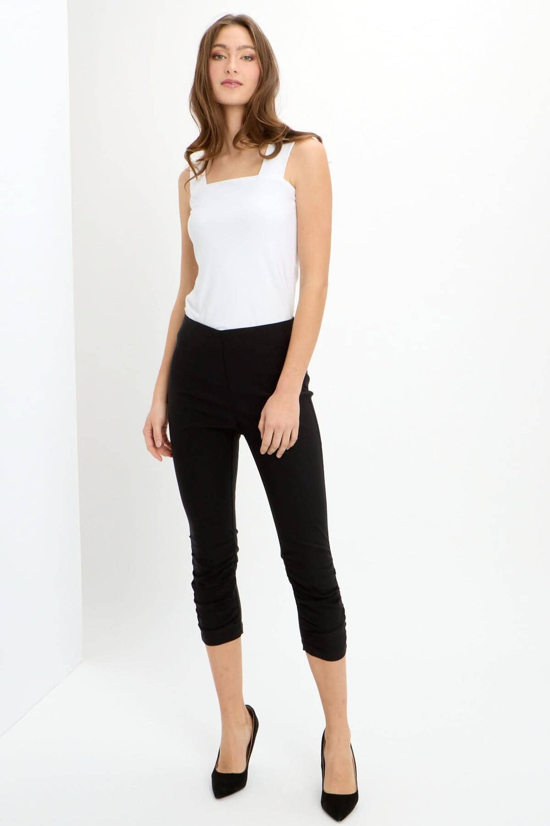 Pantalon capri noir avec ceinture extensible, fronces devant, et coupes arrière, porté avec un débardeur blanc.