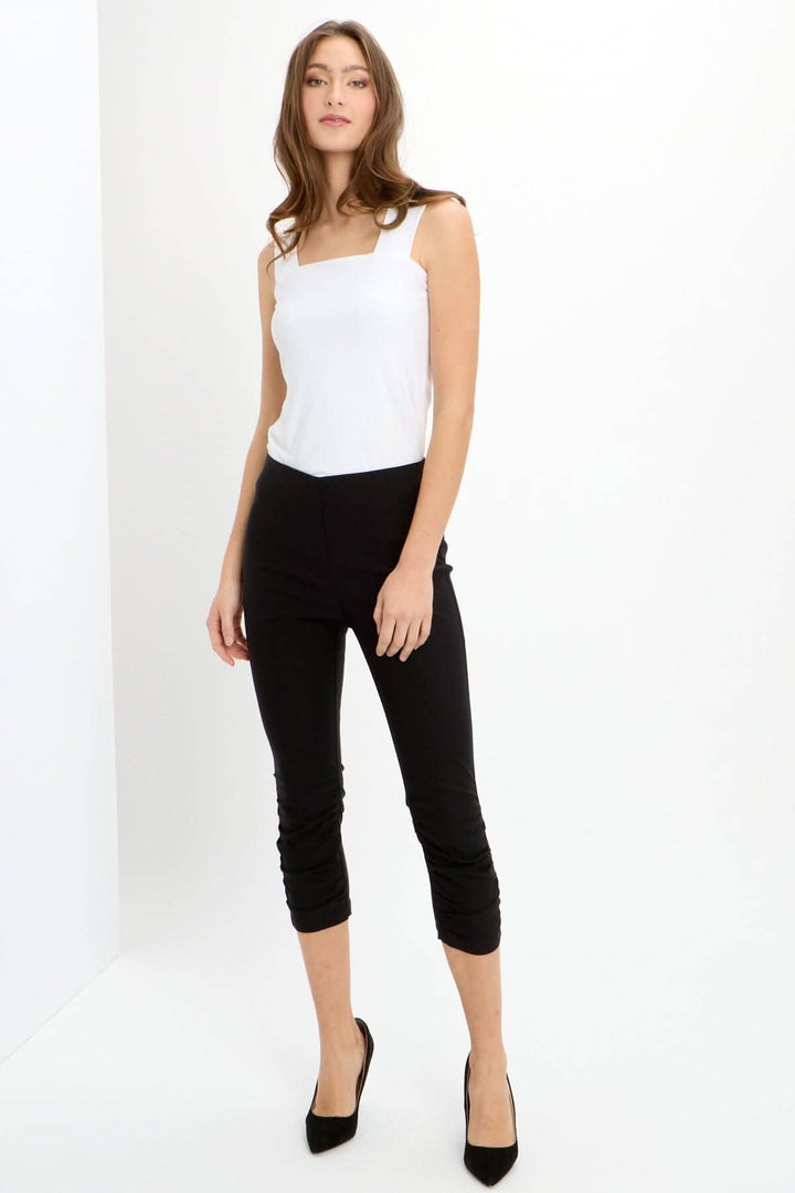 Pantalon capri noir avec ceinture extensible, fronces devant, et coupes arrière, porté avec un débardeur blanc.