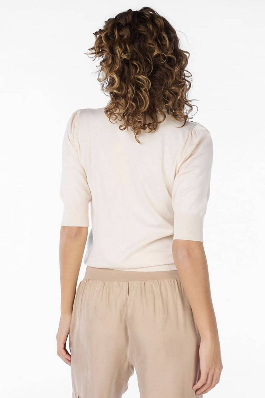 Femme vue de dos portant un pull crème et un pantalon beige, cheveux bouclés.