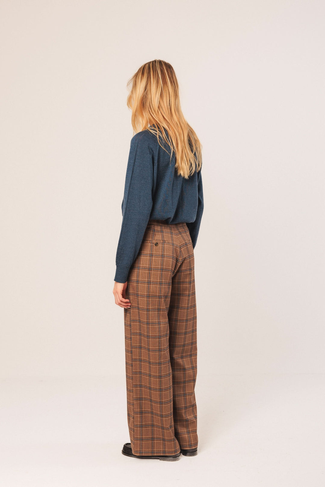 Pantalon à carreaux marron avec taille haute et coupe large, porté avec un chandail uni derrière.