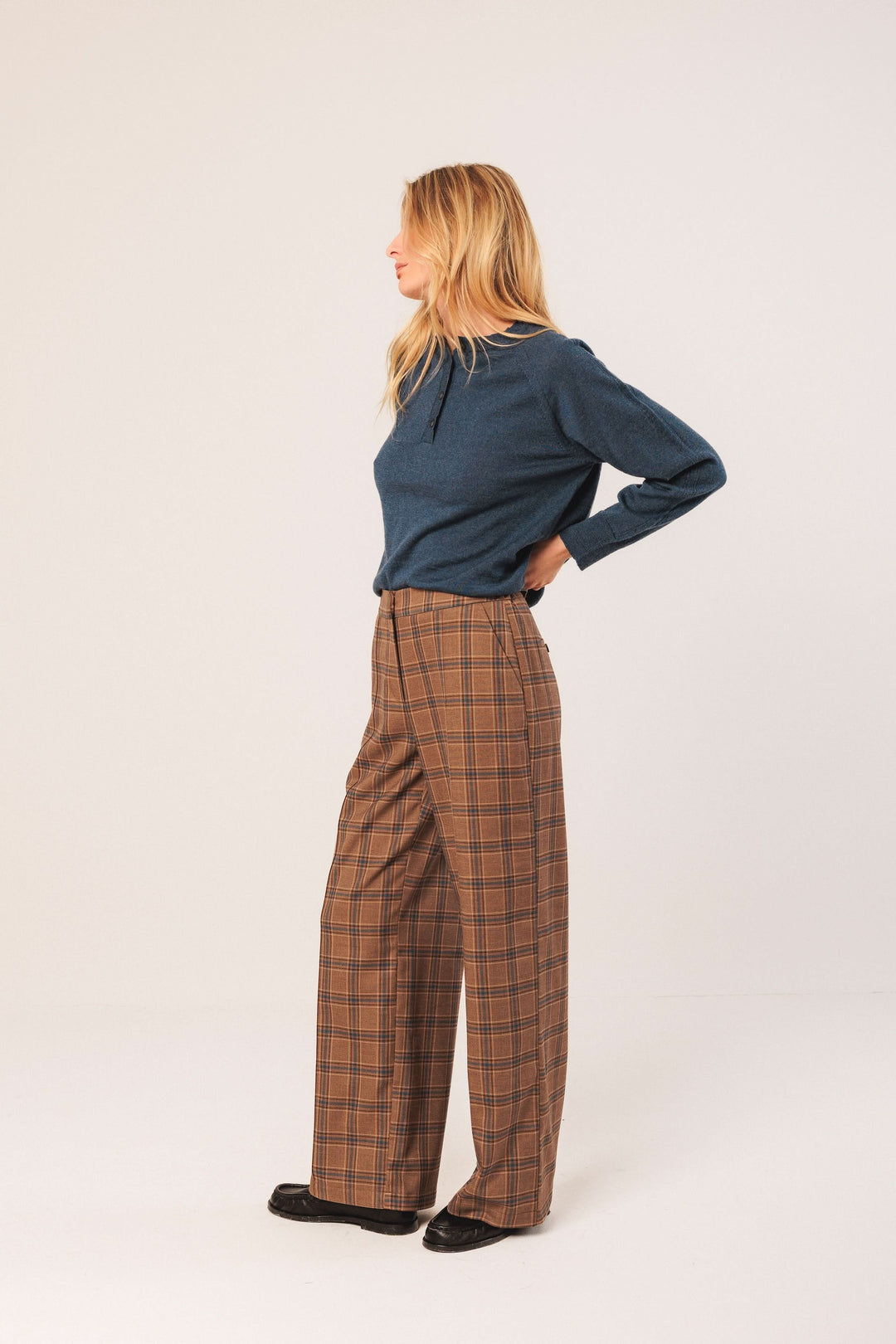 Femme portant un pantalon à carreaux large et fluide, avec un chandail bleu uni, en pose latérale.
