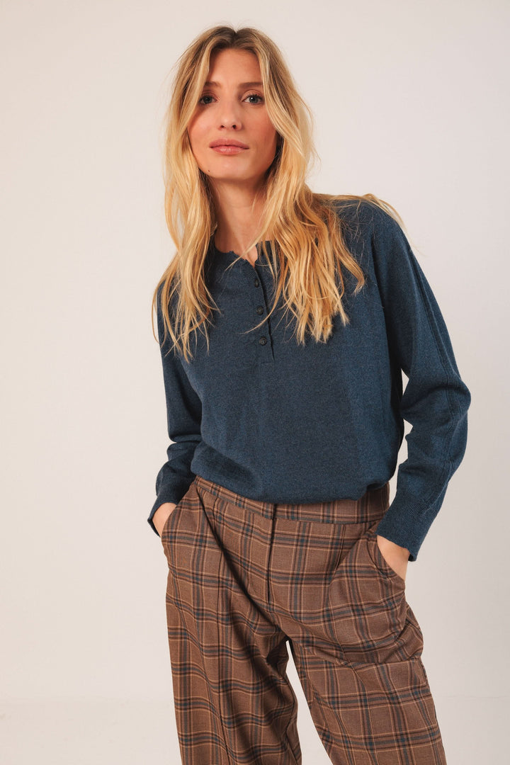 Femme portant un pantalon à carreaux élégant et confortable avec un haut bleu, coiffure blonde, style moderne et chic.