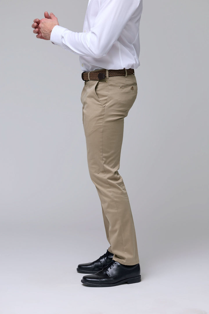 Homme portant un pantalon chino ajusté beige, style professionnel et décontracté, avec chemise blanche et ceinture.
