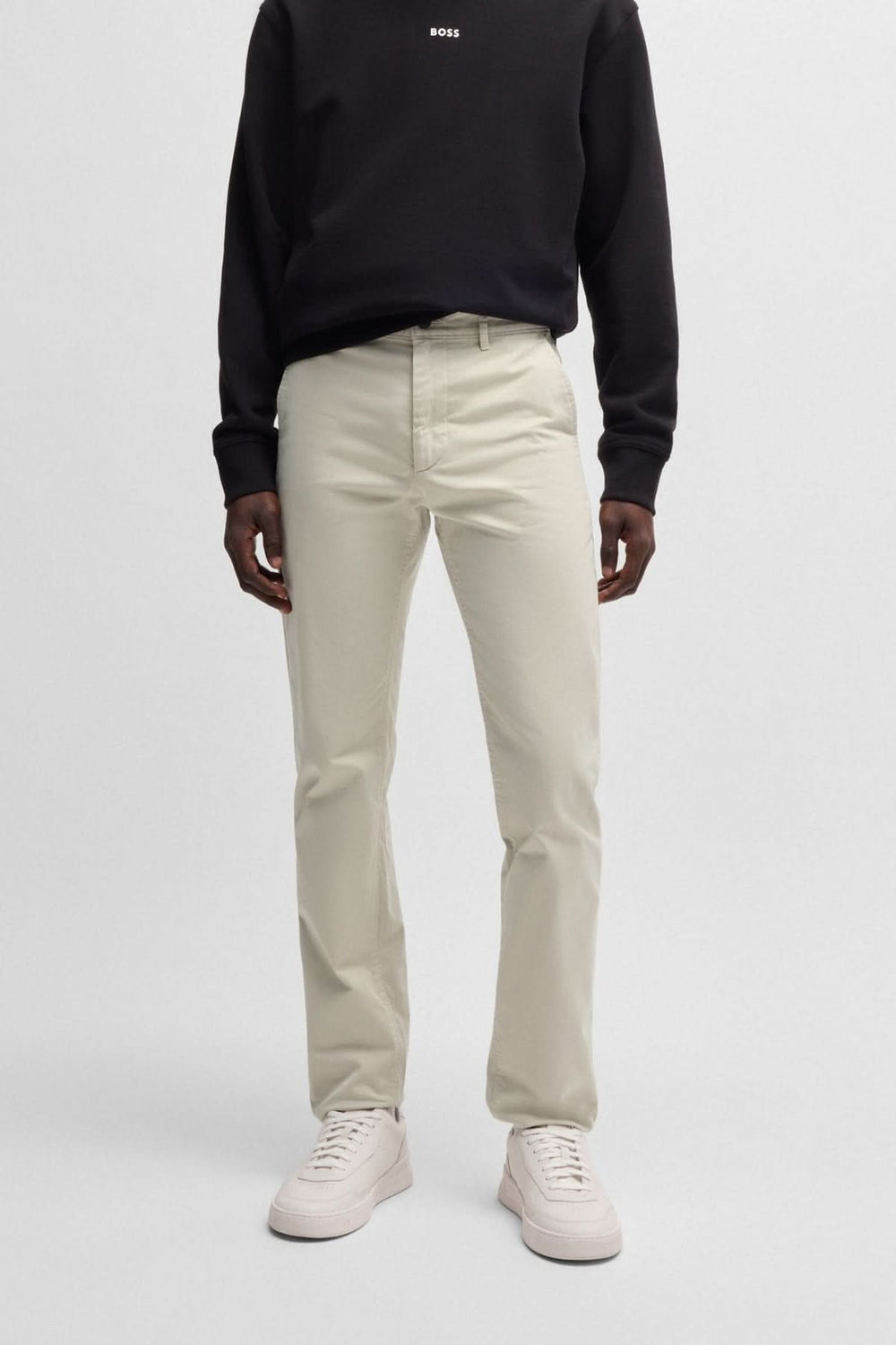 Pantalon chino slim beige porté par un homme, associé à un sweat noir et des baskets blanches.