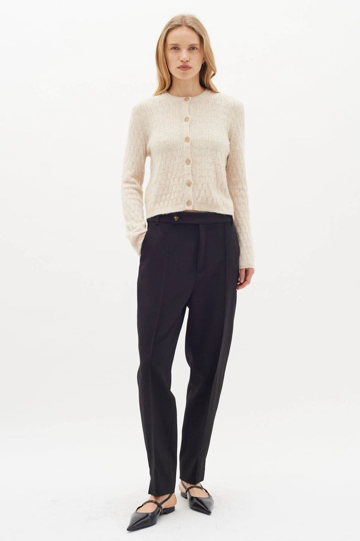 Femme portant un pantalon classique noir avec un pull crème à boutons, look élégant et raffiné.