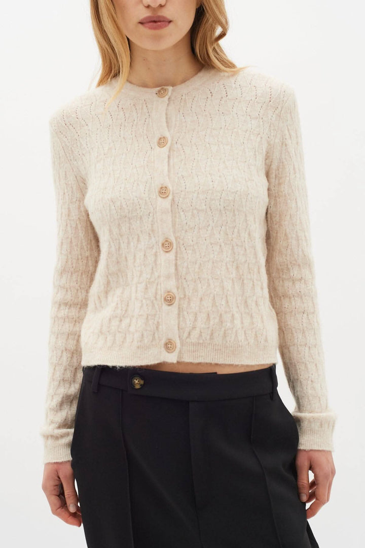 Gilet à boutons en laine beige, avec texture tricotée, porté sur un pantalon noir, style chic et féminin.