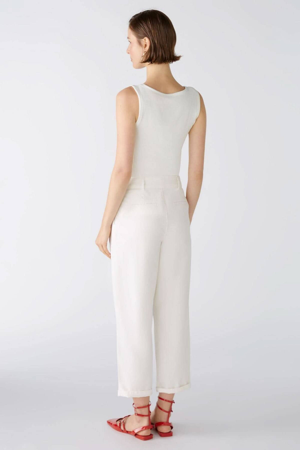 Femme vue de dos portant un pantalon coupe ample blanc, associé à un débardeur et des sandales rouges.