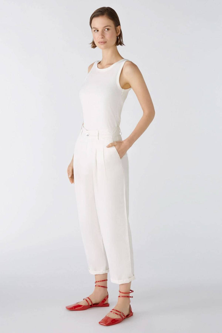 Femme en pantalon ample blanc, débardeur élégant, chaussures rouges, style décontracté, pose sur fond clair.