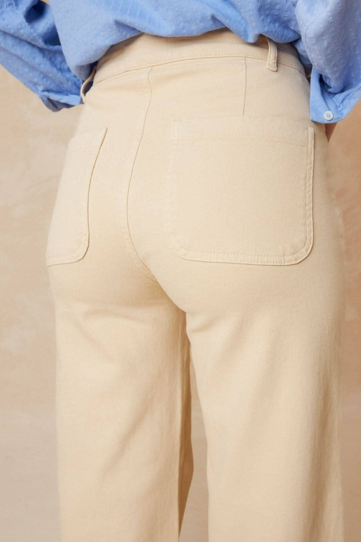 Détails arrière d'un pantalon droit beige avec taille haute et poches, porté avec une chemise bleu clair.