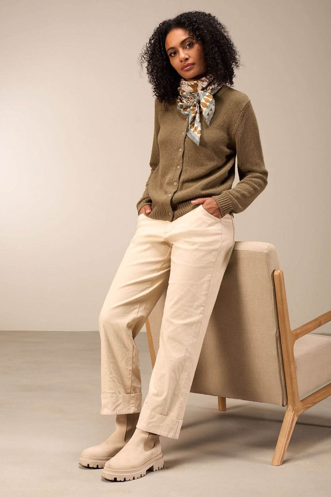 Pantalon droit beige pour un style décontracté avec chandail en maille et bottines, femme posant confortablement assise.