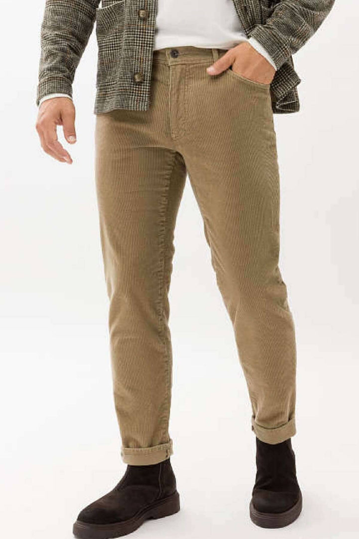 Pantalon en corduroy pour homme, coupe droite beige, porté avec un haut blanc et des bottes noires.