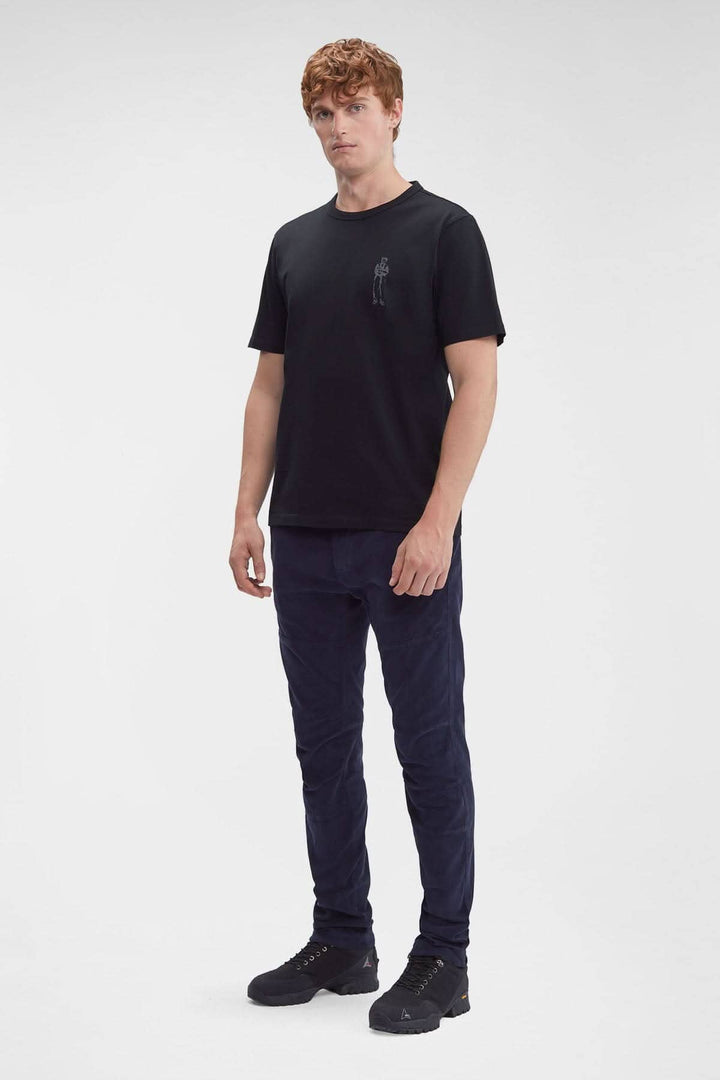 Homme portant un pantalon en corduroy et un t-shirt noir, posé sur fond blanc.